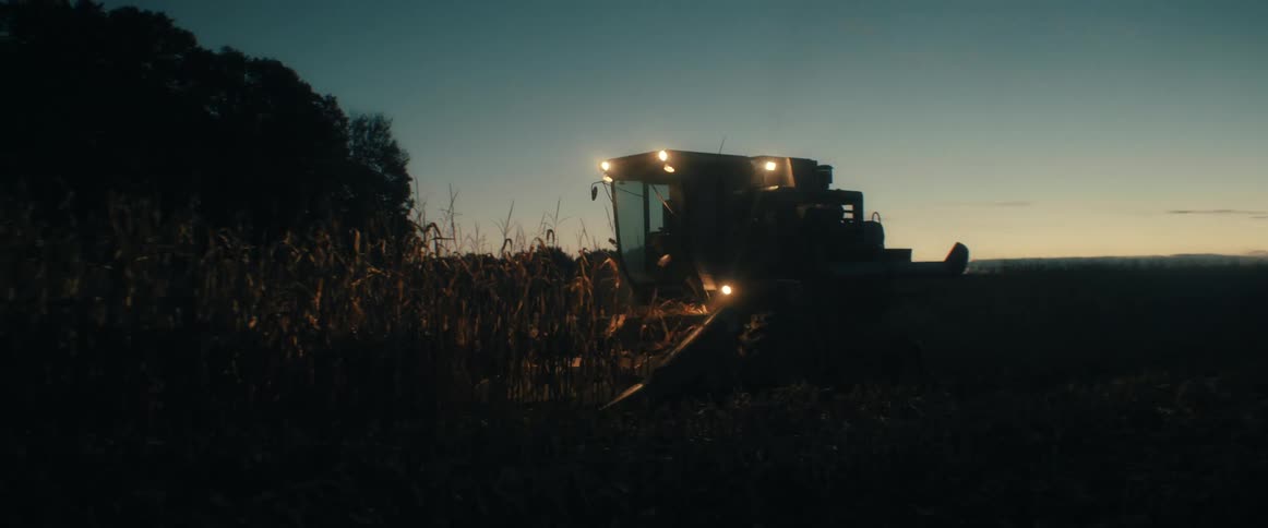 With its bright lights cutting through the darkness, a combine harvester works late into the night harvesting a rural corn field