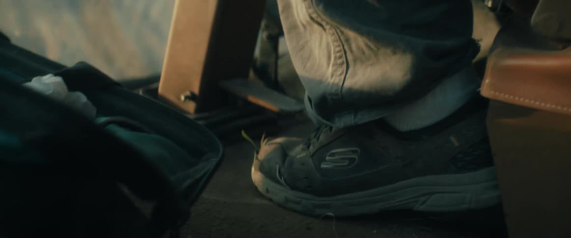 A close-up of a laborer's worn-out sneaker resting on the floor of a piece of heavy machinery