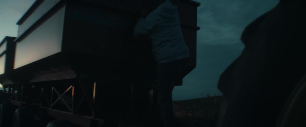 Slow motion shot of a man in a hoodie climbing down a piece of farm equipment at dusk