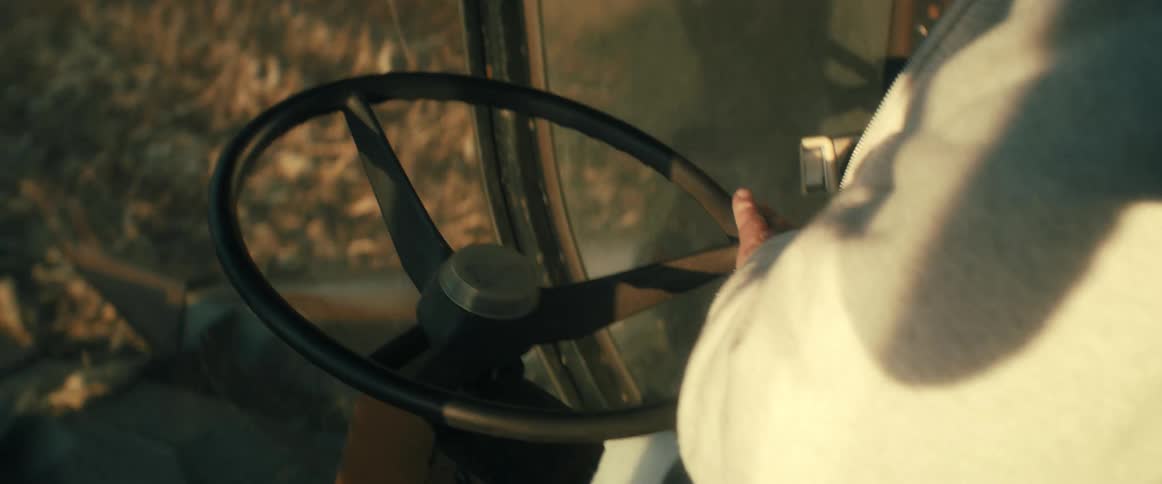 Close-up of a farmer's hands steering a combine harvester through a field during the golden hour
