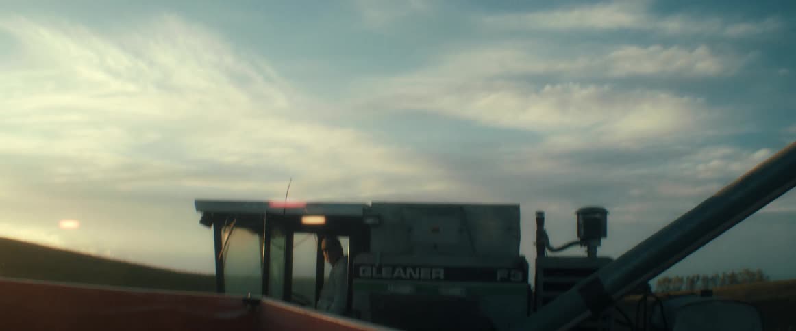 From inside a grain cart, a combine harvester unloads its grain and drives away into the sunset