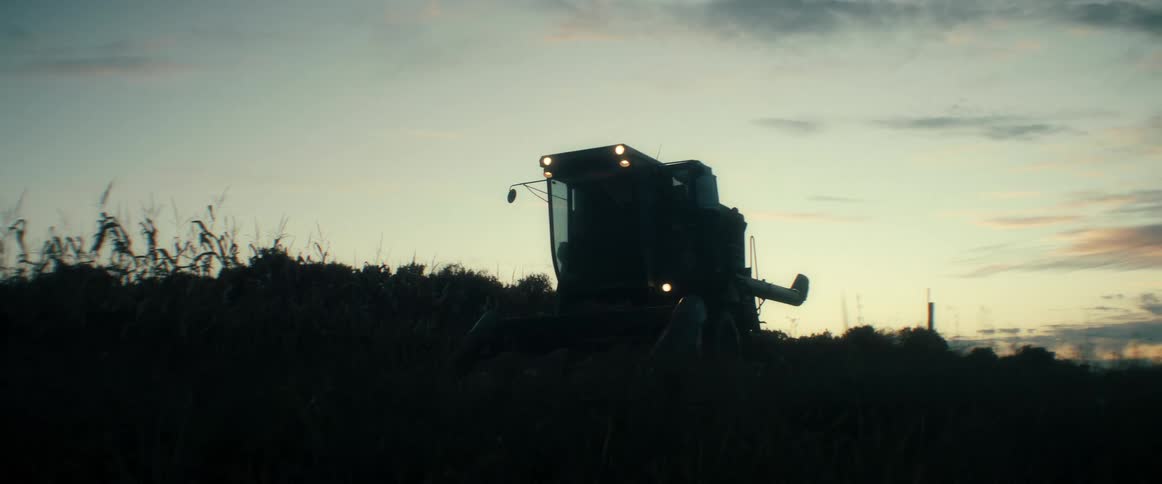 A farmer climbs into a combine harvester to begin harvesting a cornfield at dawn