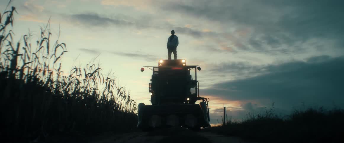 Silhouette of a farmer standing proudly on top of a combine harvester at sunset in a rural cornfield