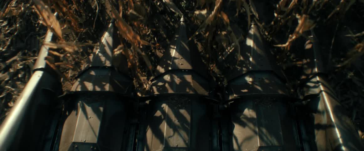 An intense point-of-view shot shows the metal blades of a combine harvester mowing down dry corn stalks during the autumn harvest