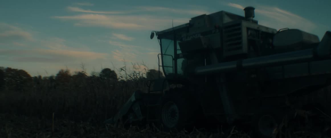 A combine harvester tirelessly works through a vast cornfield, gathering the autumn crop as the sun sets