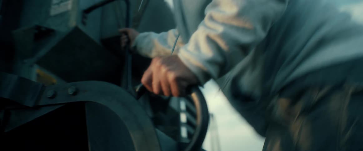 A farmer wearing a hoodie climbs into the cab of his farm equipment in a field in slow motion