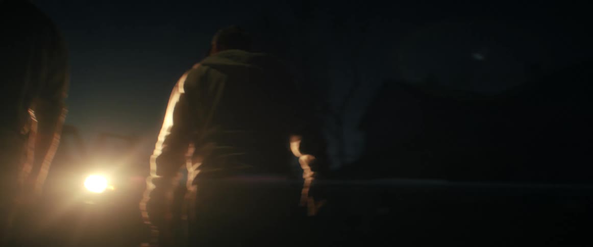 A man walks into the bright headlights of a car during a mysterious nighttime meeting with another man
