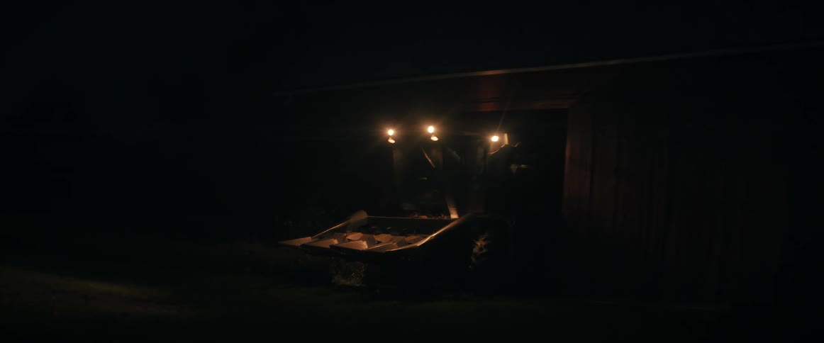 A combine harvester's headlights illuminate the darkness as it sits parked inside a red barn late at night
