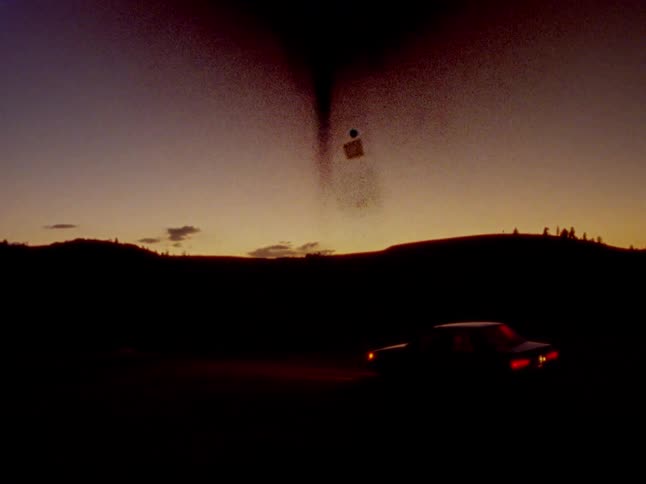 An ominous dark vortex with a floating cube appears in the twilight sky above a parked car in a desolate landscape