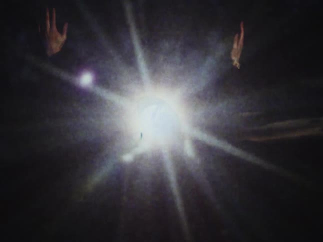 A mysterious figure raises their hands into a blinding, star-like light in this abstract vintage-style clip