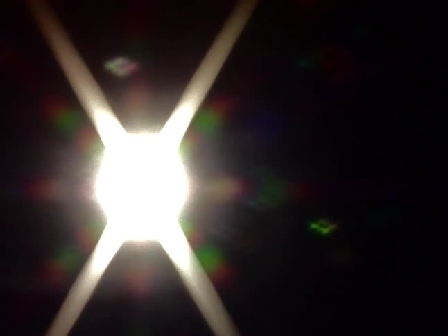An abstract close-up of a bright, starburst light flaring and expanding to fill the dark frame