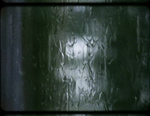Vintage super 8 film shows an abstract close-up of rain streaking down a dark green, textured window