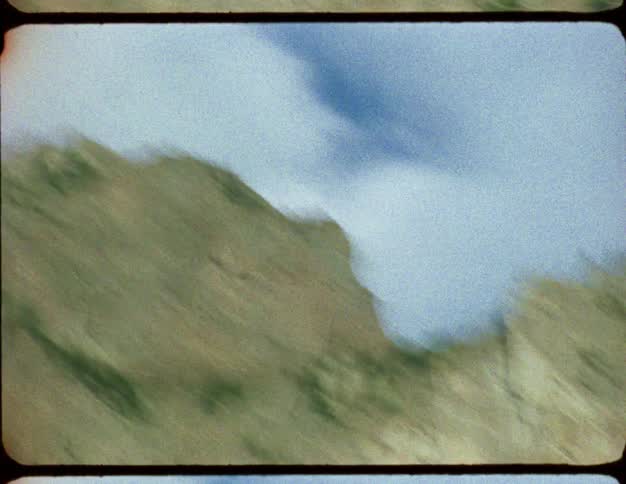 Vintage 8mm footage captures a blurry, fast-moving view of green mountainsides and rocky cliffs passing by