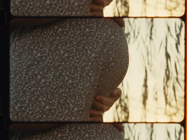 An expectant mother gently holds her baby bump in this intimate, vertical close-up with a nostalgic vintage film aesthetic