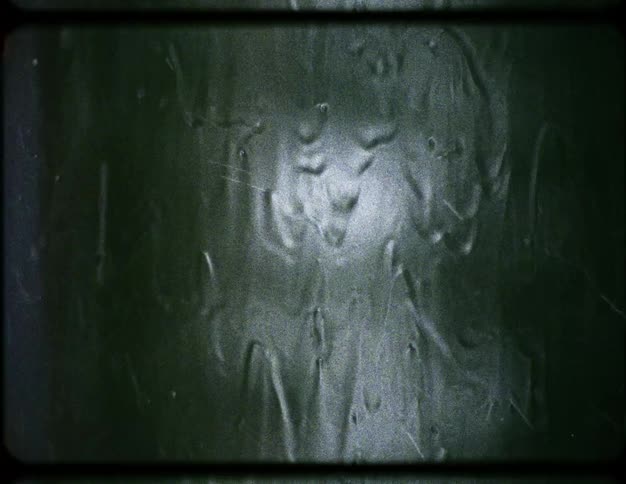 Vintage film footage shows a close-up of rain running down a dark, moody window pane