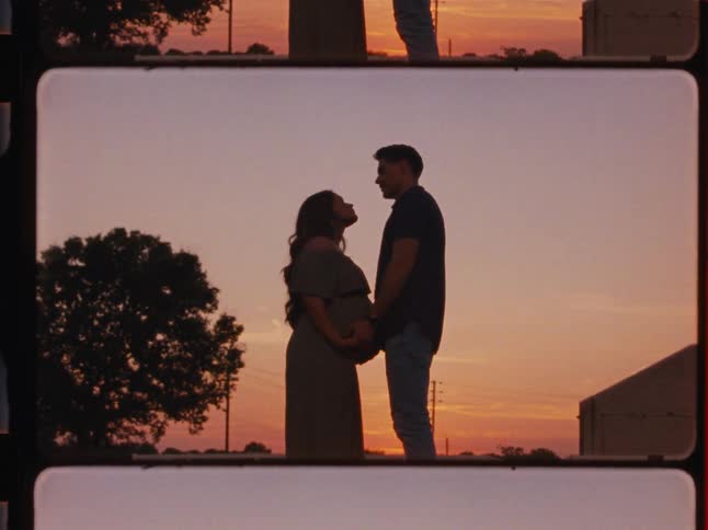 A romantic silhouette of a pregnant woman and her partner holding hands and lovingly looking at each other during a beautiful sunset, framed in a vintage film strip