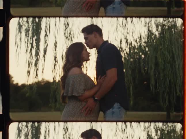 A loving husband kisses his pregnant wife's forehead as they embrace under a willow tree during a beautiful golden hour sunset, captured in a nostalgic film strip style