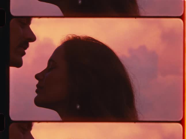 A man gently kisses a woman on the forehead, silhouetted against a romantic sunset sky in this vintage 8mm film style clip
