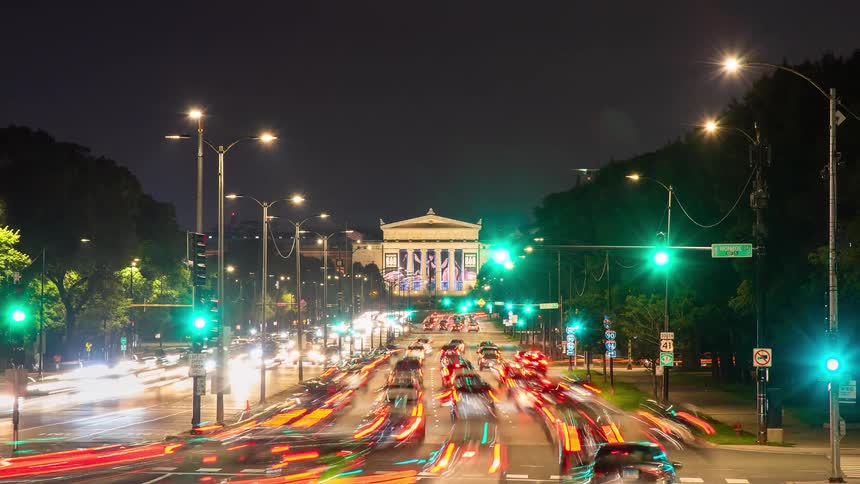 A vibrant nighttime timelapse captures the constant flow of traffic creating colorful light streaks on a Chicago boulevard leading to the Field Museum