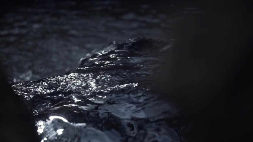 Shimmering highlights dance across the surface of dark, flowing water in a moody slow-motion shot