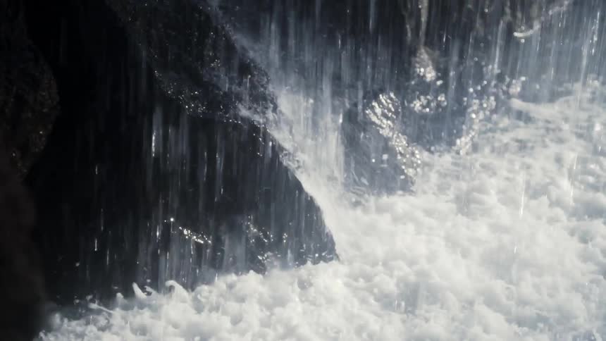 Slow-motion close-up of a powerful waterfall cascading over wet, dark rocks