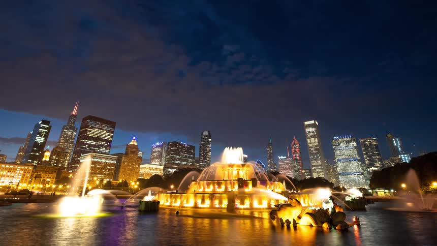 A vibrant timelapse of Chicago's Buckingham Fountain performing a colorful light and water show against the illuminated city skyline at night