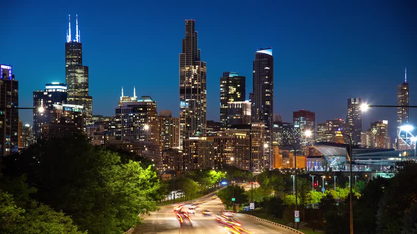 A stunning time-lapse of the iconic Chicago skyline at night, with vibrant light trails from traffic on a busy highway in the foreground