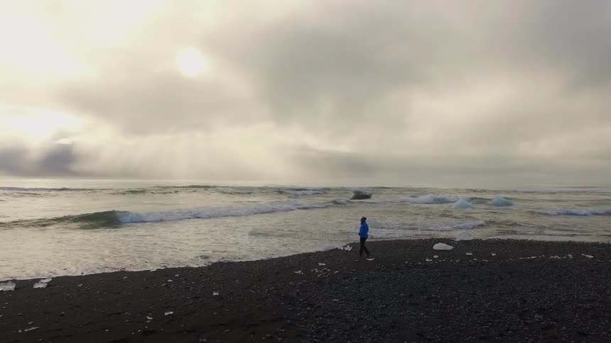 Person walks alongside a beach with large ocean waves