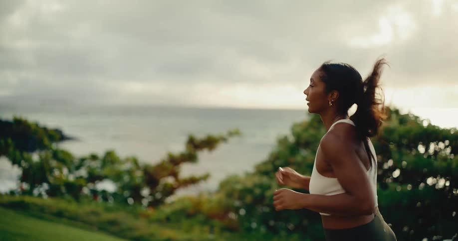 Slow motion side view of a beautiful Black woman running outdoors with the ocean in the background at sunset
