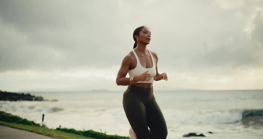 An athletic woman runs in slow motion along a beautiful tropical coastline on a cloudy morning