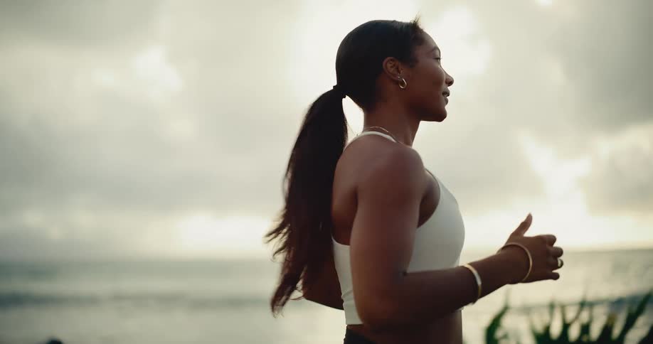 An athletic woman with a ponytail jogs gracefully along the coastline at sunrise in slow motion