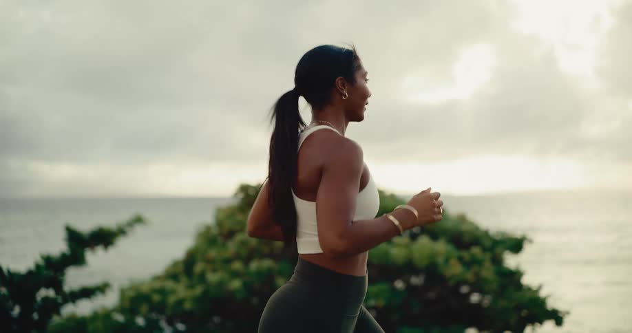 Slow motion side view of a fit woman running along a scenic coastal path at sunrise