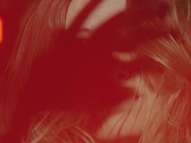 A woman's face is obscured by a hand's shadow under an intense red light, followed by a bright yellow film burn transition
