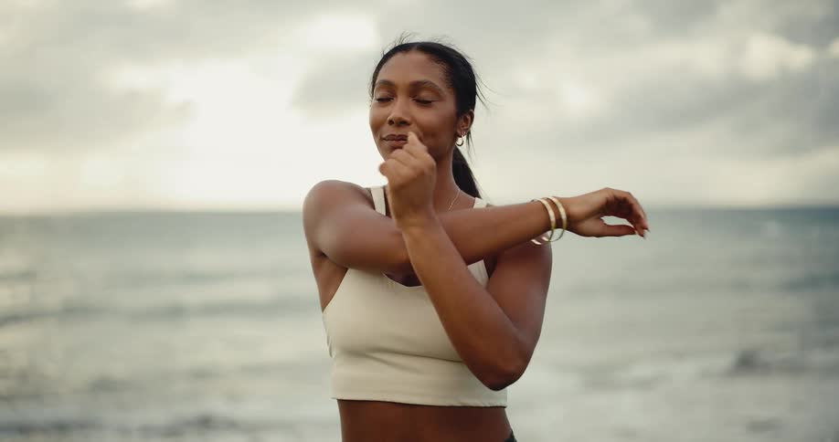 Beautiful athletic woman stretching her arms before her morning workout by the ocean