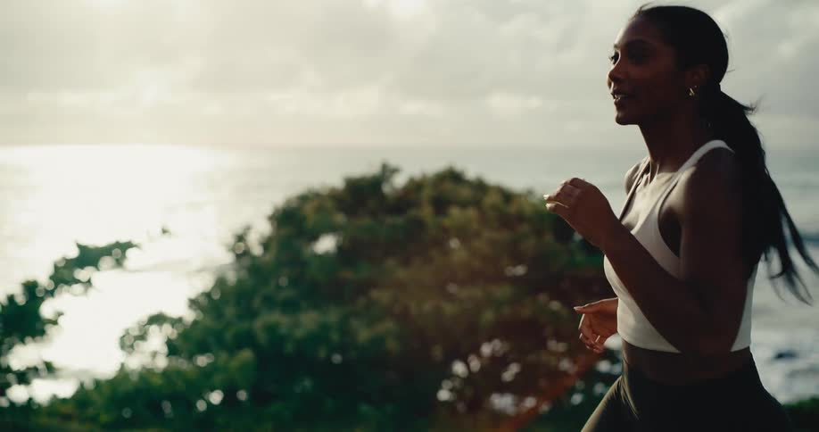 Slow motion close-up of a fit woman running along a scenic coastal trail at sunrise