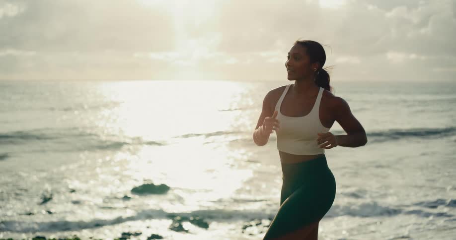 A fit woman jogs along the ocean coastline during a beautiful sunrise in slow motion