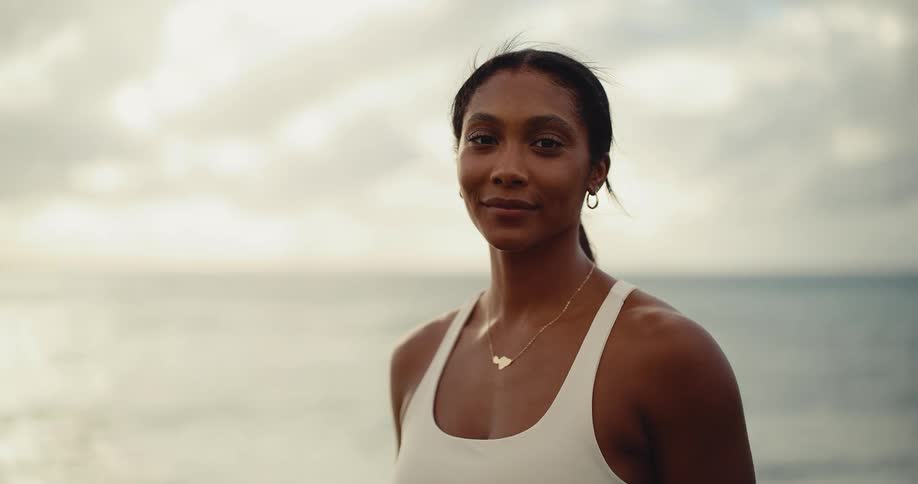 Close-up portrait of a beautiful and athletic woman smiling confidently on the beach at sunrise