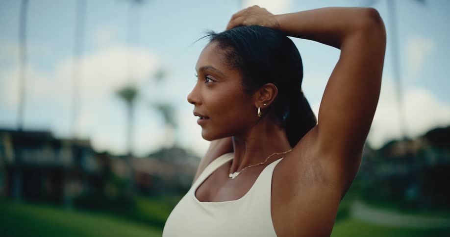 Slow motion close-up of a beautiful athletic woman stretching her arms while warming up outdoors in a tropical setting