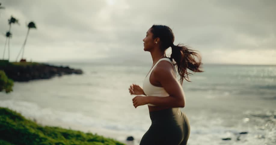 Athletic woman runs along a scenic tropical coastline at sunrise in slow motion