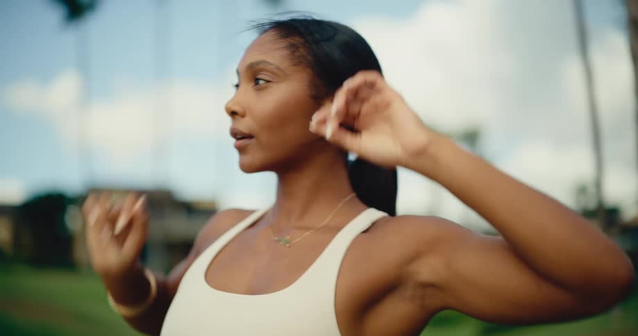 A beautiful, fit woman in a white athletic top mindfully stretches her body in a tropical park in slow motion