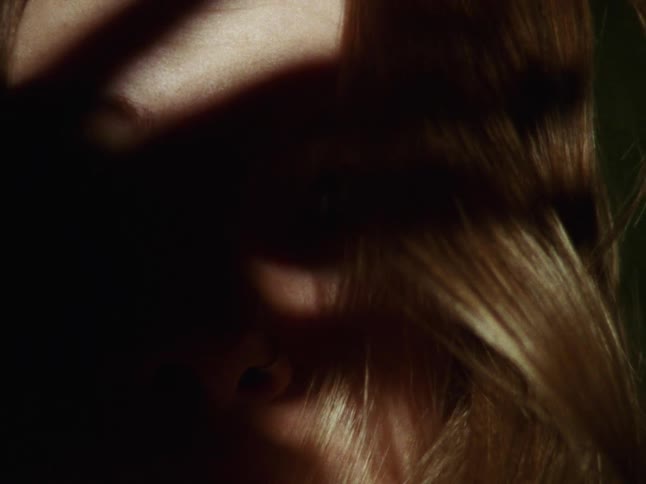 The ominous shadow of a hand falls across a woman's face in a tense and mysterious close-up