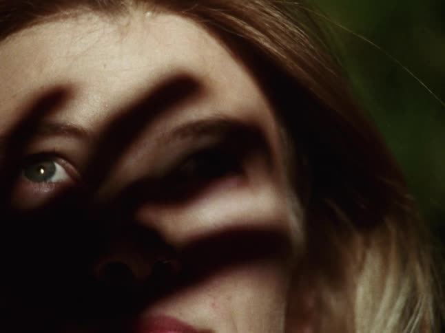 A moody and artistic close-up of a young person's face obscured by the shadow of a hand