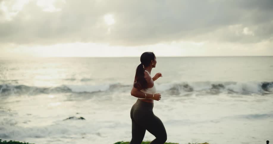 A fit woman runs along the ocean coastline at sunrise in slow motion