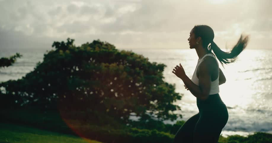 A beautiful athletic woman runs along a coastal path with the ocean in the background at sunrise in slow motion