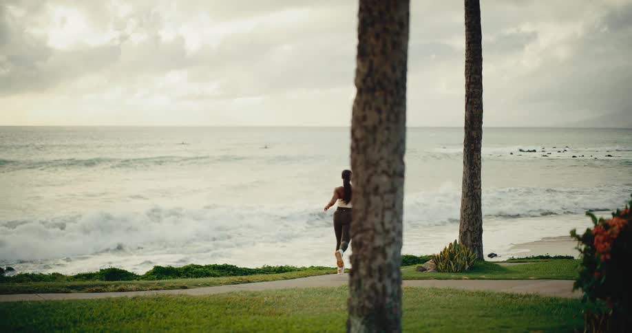 An athletic woman jogs on a scenic path next to the ocean in slow motion