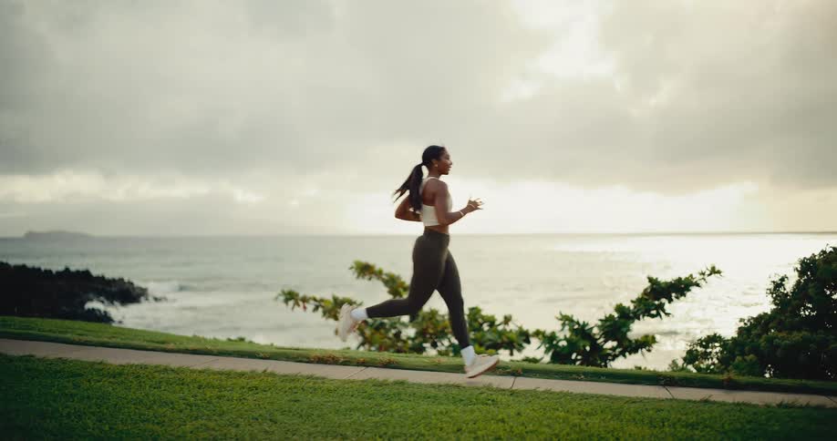 Slow motion side view of a fit woman running along a scenic coastal path next to the ocean at sunrise