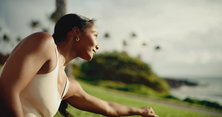 A serene woman stretches her muscles in a tranquil coastal park during a beautiful golden hour workout