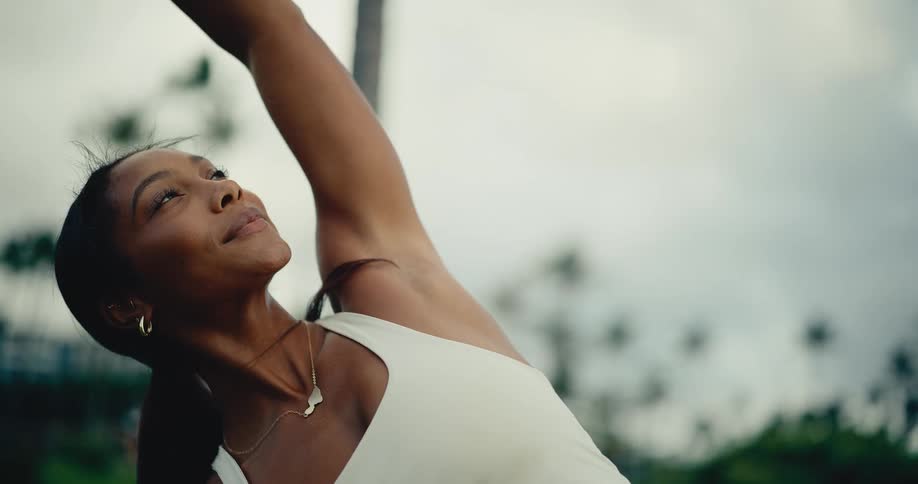 A close-up slow-motion shot captures a serene woman performing a graceful yoga stretch in a tranquil outdoor park