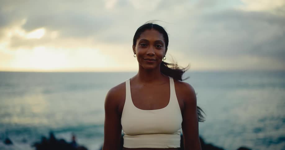 Portrait of a beautiful athletic woman smiling peacefully by the ocean at sunset with her hair blowing in the wind