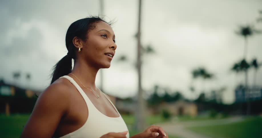A determined athletic woman in workout clothes runs in slow motion through a beautiful tropical park